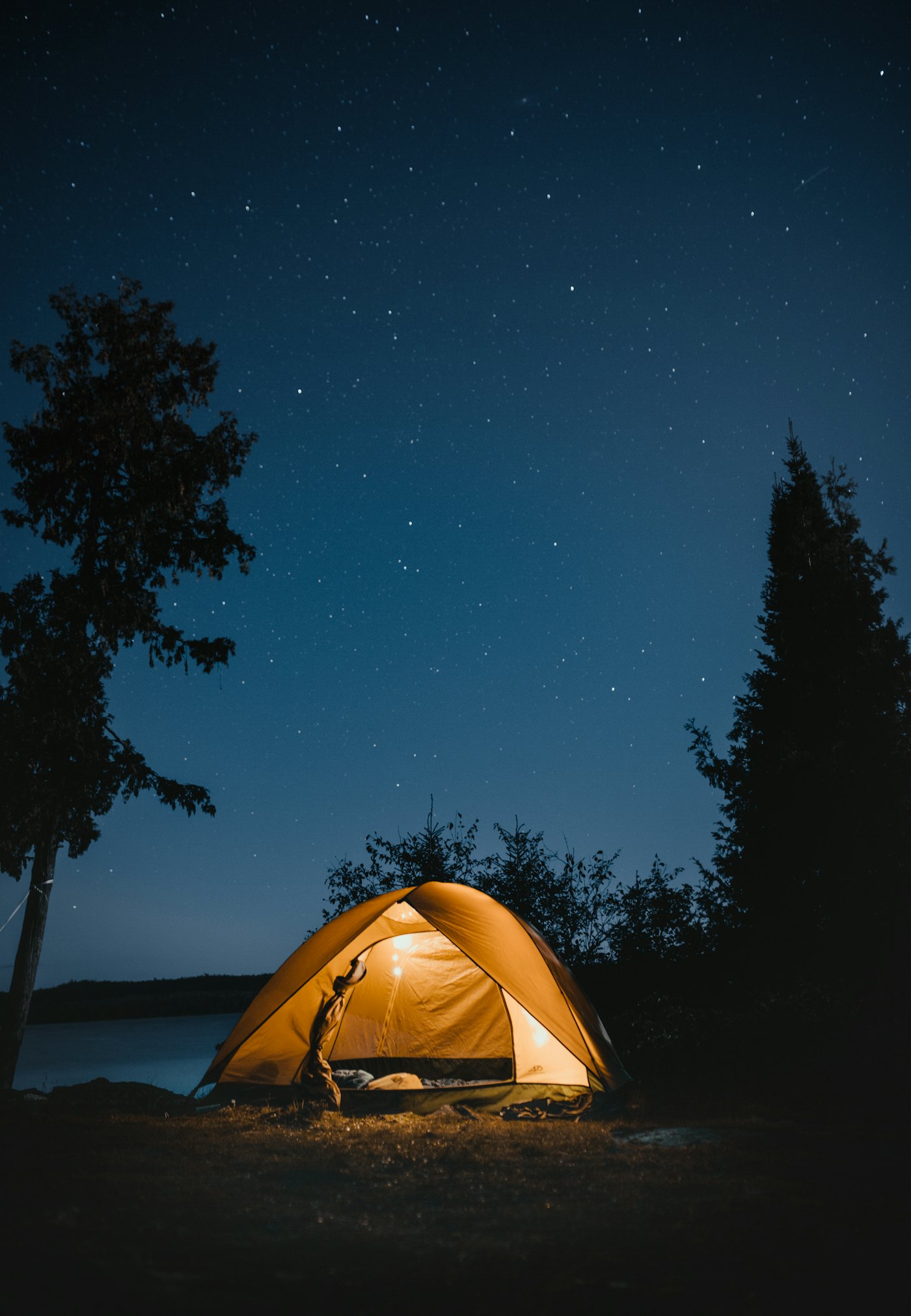 Lit tent at a lakeside campsite under the stars